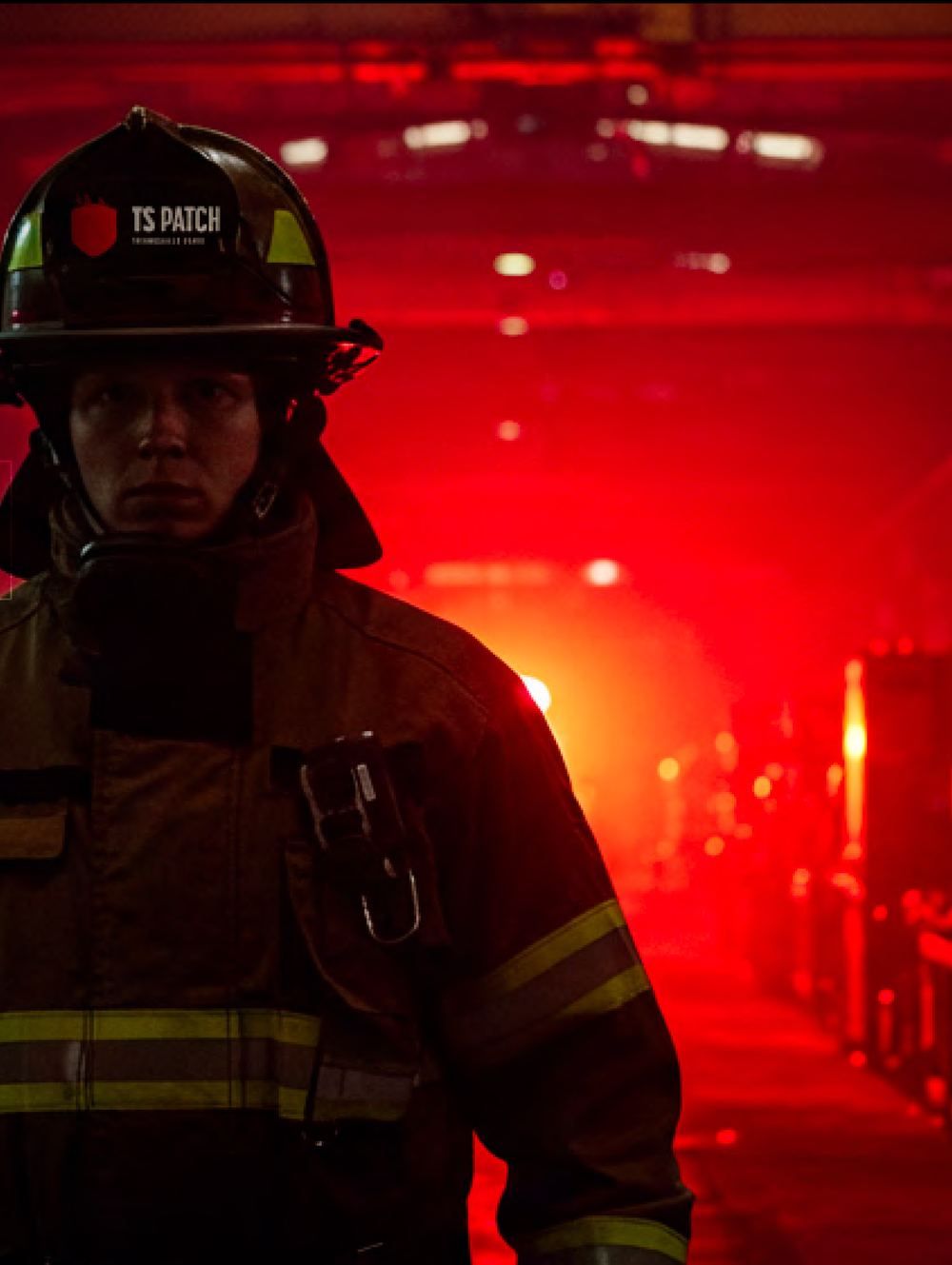 A firefighter in a TS Patch branded helmet standing in a corridor lit by red emergency light